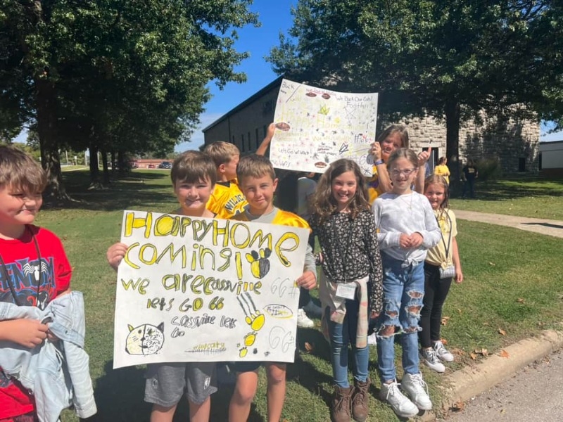 students standing outside of the school during a beautiful day. students are smiling and holding up signs